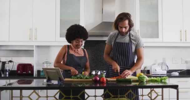 Couple mixte portant des tabliers hachant des légumes ensemble dans la cuisine à la maison — Video