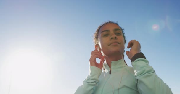 Afroamerykanka w sportowej odzieży, nosząca słuchawki w słoneczny dzień. — Wideo stockowe