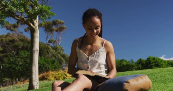Afričanky americká žena sedí na trávě čtení knihy v parku — Stock video