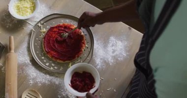 Afro-Amerikalı adam pizza yapıyor. Mutfağa domates saçıyor. Karantina süresince evde tek başına kalarak eğleniyor. 