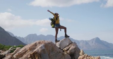 Dağlarda yürürken kolları açık kayaların üzerinde duran Afrikalı Amerikalı kadın.