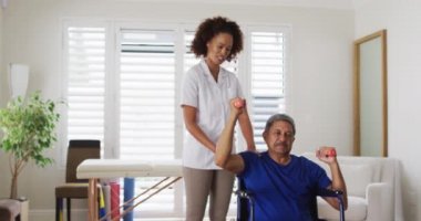 Karışık ırk kadın fizyoterapist yaşlı adama halterleri kullanarak egzersiz yaptırıyor.