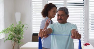 Karışık ırk kadın fizyoterapist yaşlı adamın egzersiz bandını kullanmasına yardım ediyor.