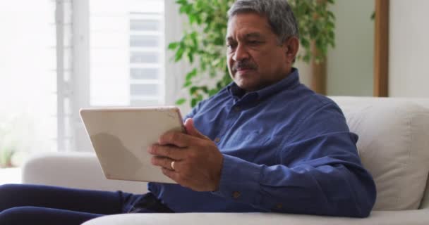 Senior smíšené rasy muž pomocí tabletu v obývacím pokoji — Stock video