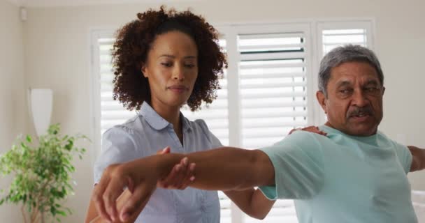 Melez kadın fizyoterapist, yaşlı adamın kollarını açmasına yardım ediyor. — Stok video