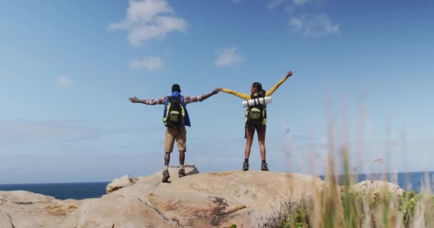 Zadní pohled na africký americký pár stojící na skalách s pažemi dokořán při trekking — Stock video