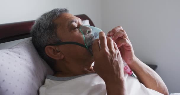 Hombre de raza mixta mayor acostado en la cama en casa usando un ventilador de máscara facial — Vídeo de stock