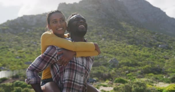 African american man giving piggyback ride to his wife while trekking in the mountains — Stock Video