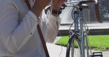 Bisikletli Afrikalı Amerikalı kadın şehir parkında kulaklık takıyor. Dijital göçebe şehirde dolaşıyor..