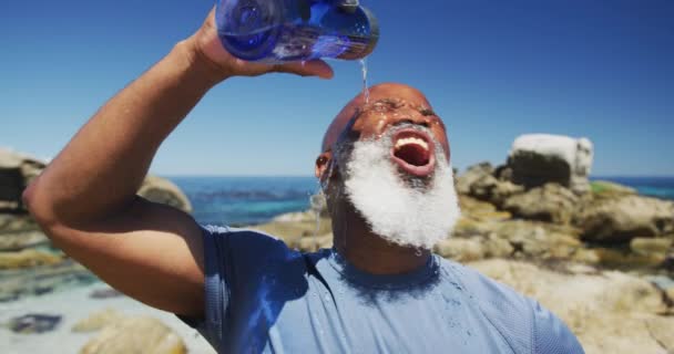 Senior African American Man Exercising Pouring Water Face Rocks Sea — Stock Video