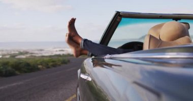 Afro-Amerikalı kadın ayakları üstü açık arabanın camında oturuyor. Yolculuk ve macera konsepti