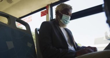 Otobüste otururken dizüstü bilgisayar kullanarak yüz maskesi takan Afrikalı Amerikalı son sınıf öğrencisi. Coronavirus covid-19 salgınında hijyen ve sosyal mesafeler.