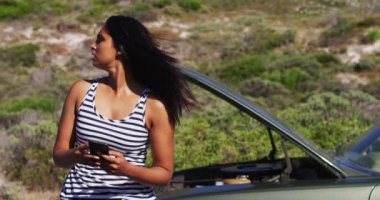 Yolda bozuk arabasının yanında dururken akıllı telefon kullanan Afrikalı Amerikalı bir kadın. Yolculuk ve macera konsepti