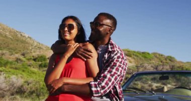 Afro-Amerikan çift yolda üstü açık arabaların yanında dururken birbirlerine sarılıyorlar. Yolculuk ve macera konsepti