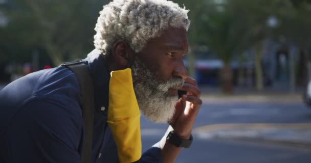 顔のマスクをしたアフリカ系アメリカ人の老人が道路上のスマートフォンで話しているのを閉じます コロナウイルスの間の衛生と社会的距離 Covid 19パンデミック — ストック動画