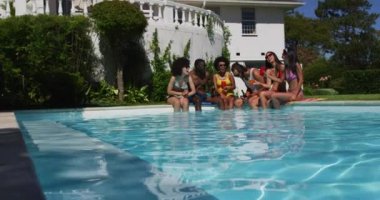 Çeşitli arkadaşlar havuz kenarında otururken içkinin tadını çıkarıyorlar. Gençlik arkadaşlığı ve havuz partisi konsepti