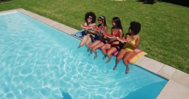 Havuz kenarında otururken karpuz yiyen bir grup farklı kızın genel görünümü. Gençlik arkadaşlığı ve havuz partisi konsepti