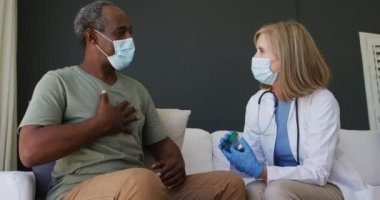Kafkas kıdemli kadın doktor elinde ilaçla yatakta erkek hastayla konuşuyor. İkisi de maske takıyor. Coronavirüs covid 19 salgını sırasında sağlık hizmetleri koruması.