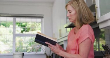 Kafkasyalı son sınıf öğrencisi kadın mutfakta durmuş kitap okuyor. Karantina süresince evde tecrit altında kalmak.