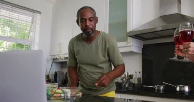 Çeşitli kıdemli çiftler mutfakta yemek hazırlıyor dizüstü bilgisayar kullanıyor ve şarap içiyor. Karantina süresince evde tecrit altında kalmak.