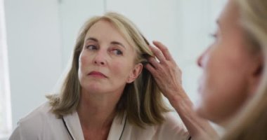 Kafkasyalı son sınıf öğrencisi, banyo aynasına bakıyor ve yüzünü inceliyor. Karantina süresince evde tecrit altında kalmak.