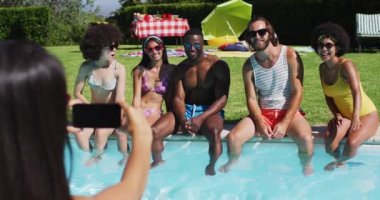 Bir grup farklı arkadaş havuz kenarında otururken bir resim için poz veriyorlar. Gençlik arkadaşlığı ve havuz partisi konsepti