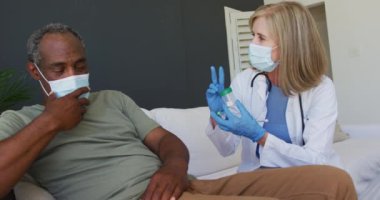 Kafkas kıdemli kadın doktor yatakta erkek hastayla konuşuyor. İkisi de maske takıyor. Coronavirüs covid 19 salgını sırasında sağlık hizmetleri koruması.