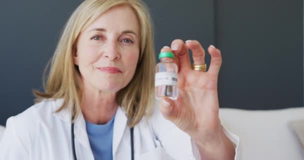 カメラと笑顔にコロナウイルスワクチンのバイアルを保持白人のシニア女性医師 コロナウイルスによる医療保護は19のパンデミックをもたらしました — ストック動画