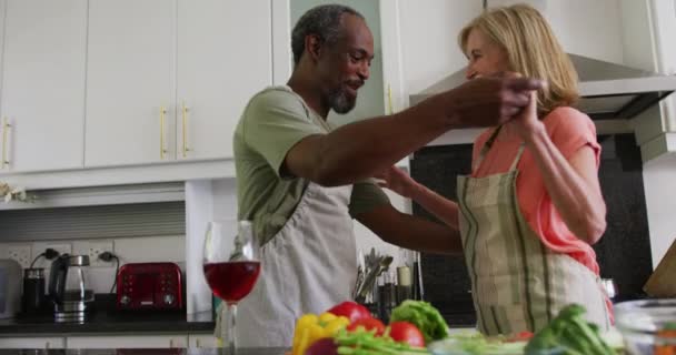 台所で食べ物を準備しながら エプロンを身に着けている多様なシニアカップル 隔離されたまま家にいると — ストック動画