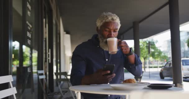 Orang Senior Afrika Amerika Menggunakan Smartphone Sambil Minum Kopi Duduk — Stok Video