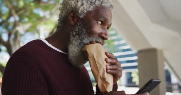 African American Senior Man Having Snack Using Smartphone Corporate Park — Stock Video