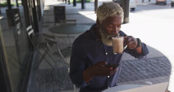 Orang Senior Afrika Amerika Menggunakan Smartphone Sambil Minum Kopi Duduk — Stok Video