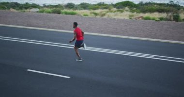 Afrika kökenli Amerikalı bir adam dışarıda egzersiz yapıyor. Sahil yolunda koşuyor. Fitness eğitimi ve sağlıklı açık hava yaşam tarzı..