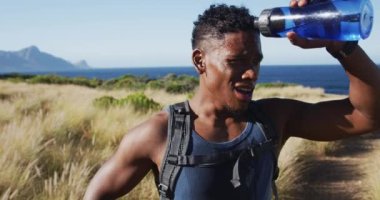 Afrika kökenli Amerikalı bir adam sahilde açık havada egzersiz yapıyor ve içme suyu içiyor. Fitness eğitimi ve sağlıklı açık hava yaşam tarzı..