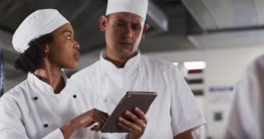 İki farklı erkek ve kadın aşçı restoran mutfağında konuşuyor ve tablet kullanıyor. Yoğun bir restoran mutfağında çalışıyorum..
