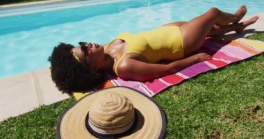 Karışık ırktan bir kadın havuz kenarında güneşleniyor. Yazın dışarıda takılır ve dinlenir..