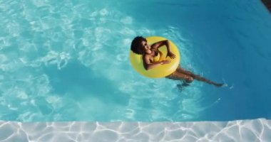 Karışık ırk kadını yüzme havuzunda şişirilebilir güneş banyosu yaparken eğleniyor. Yazın dışarıda takılır ve dinlenir..