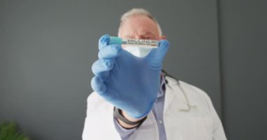 Kafkas kıdemli erkek doktorun portresi. Yüz maskesi takıyor. Elinde kovid 19 aşısı var. covid-19 aşı ve tedavi konsepti