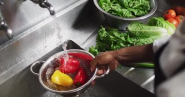 African american female chef washing vegetables in colander in restaurant kitchen. working in a busy restaurant kitchen.