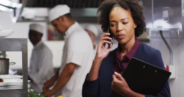 Afro-Amerikan bayan yönetici restoran mutfağında akıllı telefondan konuşuyor. Yoğun bir lokanta mutfağında çalışıyorum..