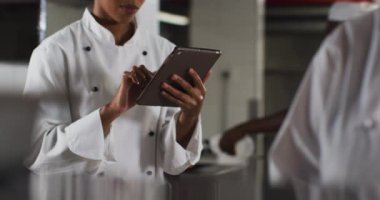 Afro-Amerikan kadın aşçı restoran mutfağında tablet kullanıyor. Yoğun bir lokanta mutfağında çalışıyorum..