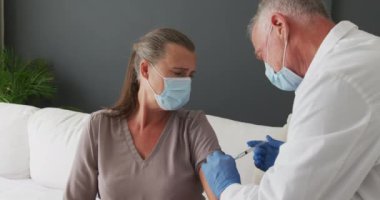 Kafkas kıdemli erkek doktor yüz maskesi takıyor ve evde kadınlara covid-19 aşısı yapıyor. covid-19 aşı ve tedavi konsepti