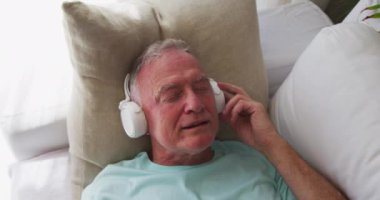 Evdeki kanepede yatarken kulaklık takan beyaz bir adam şarkı söylüyor. Karantina karantinasında tek başına evde kalmak