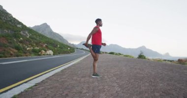 Afrika kökenli Amerikalı bir adam yolda ayakta dikilirken bacaklarını esnetiyor. fitness sporları ve sağlıklı yaşam tarzı konsepti