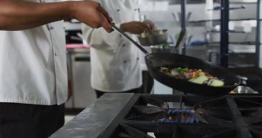 Melez erkek aşçının tavada sebze kızartmasının ortasında. Yoğun bir restoran mutfağında çalışıyorum..