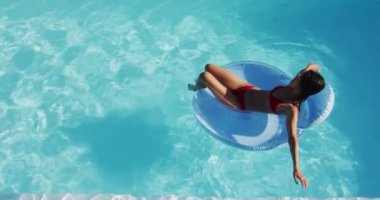 Karışık ırk kadını yüzme havuzunda şişirilebilir güneş banyosu yaparken eğleniyor. Yazın dışarıda takılır ve dinlenir..