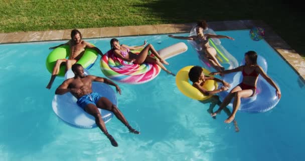 水泳プールでインフレータブルで遊ぶのを楽しんでいる友人の多様なグループ 夏には屋外でぶら下がったりリラックスしたり — ストック動画