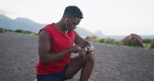 Afrykański Amerykanin Noszący Słuchawki Opaską Fitness Podczas Siedzenia Drodze Sport — Wideo stockowe