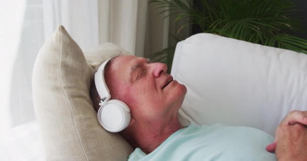 Hombre Mayor Caucásico Con Auriculares Cantando Mientras Está Acostado Sofá — Vídeo de stock