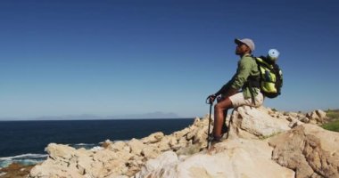 Afrika kökenli Amerikalı bir adam sahil kenarındaki bir kayanın üzerinde yürüyüş yapıyor. Fitness eğitimi ve sağlıklı açık hava yaşam tarzı..